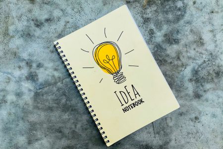 電球と「idea notebook」と書かれたノートのイメージ画像。副業に役立つクレジットカード選びのポイントを象徴