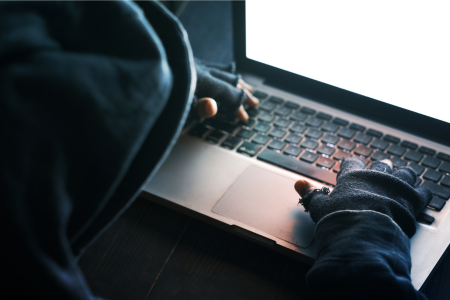 暗い部屋でパソコンを操作するフードを被ったハッカーのイラスト。クレジットカード情報の不正取得を連想させる不穏な雰囲気が特徴。